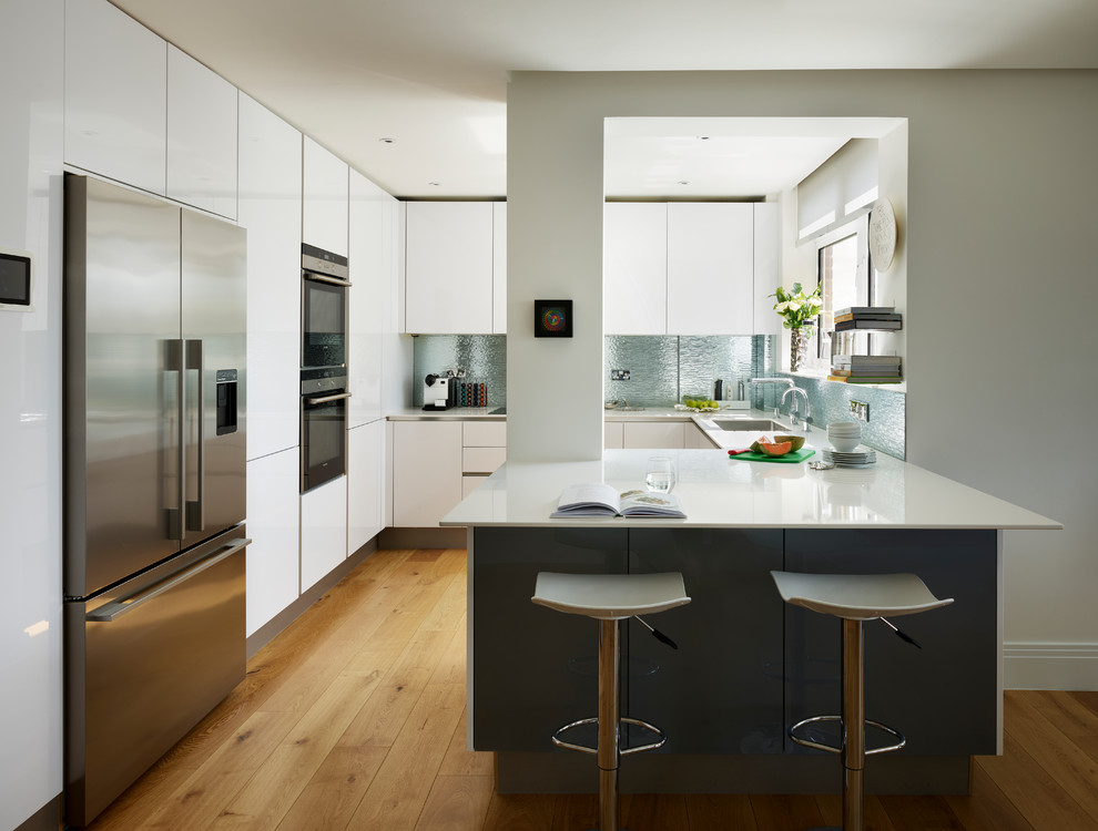 Photo of a mid-sized contemporary u-shaped kitchen in London with an undermount sink, flat-panel cabinets, white cabinets, blue splashback, metal splashback, light hardwood floors, a peninsula and brown floor.
