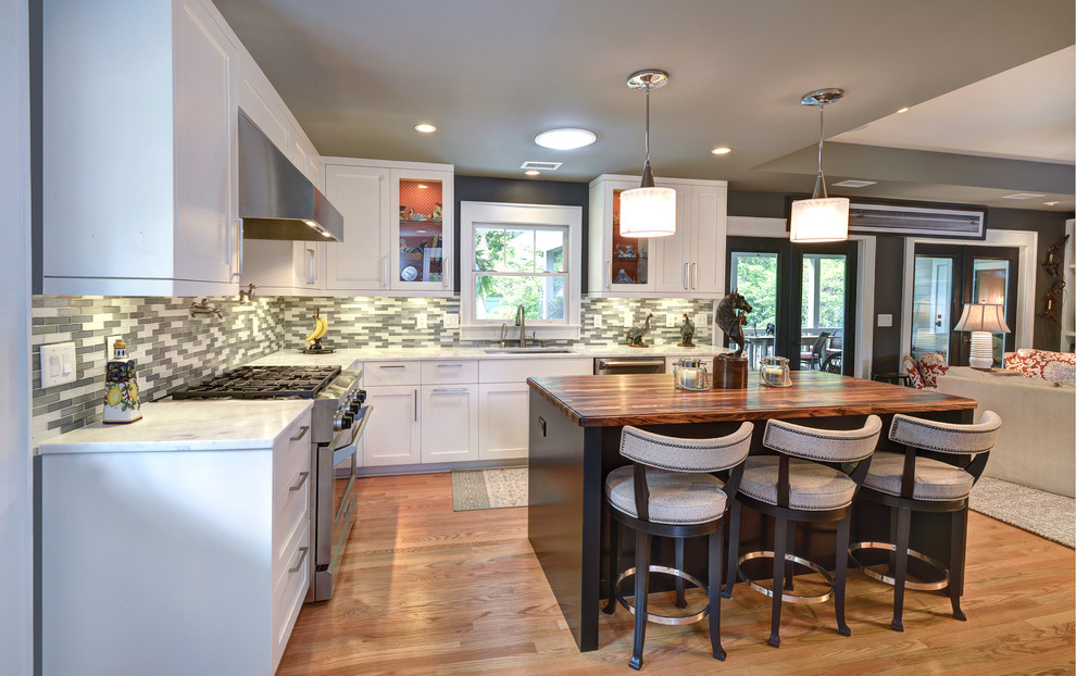 Open concept kitchen - mid-sized transitional l-shaped light wood floor open concept kitchen idea in Charleston with shaker cabinets, white cabinets, wood countertops, gray backsplash, stainless steel appliances, a single-bowl sink, glass tile backsplash and an island