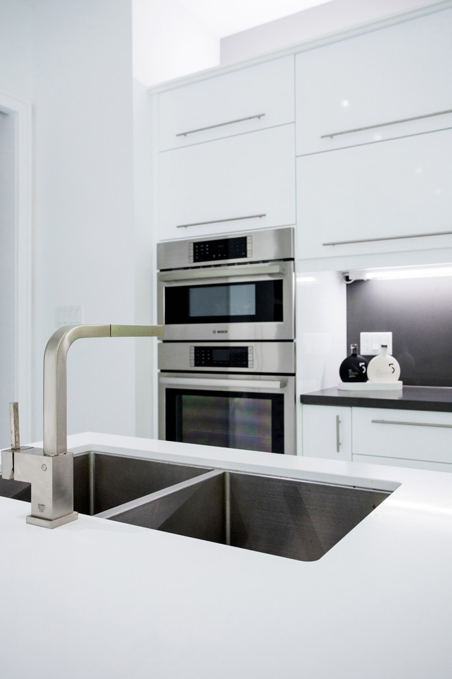 Design ideas for a large modern l-shaped eat-in kitchen in Toronto with an undermount sink, flat-panel cabinets, white cabinets, quartz benchtops, black splashback, stone slab splashback, stainless steel appliances, marble floors, with island, white floor and white benchtop.