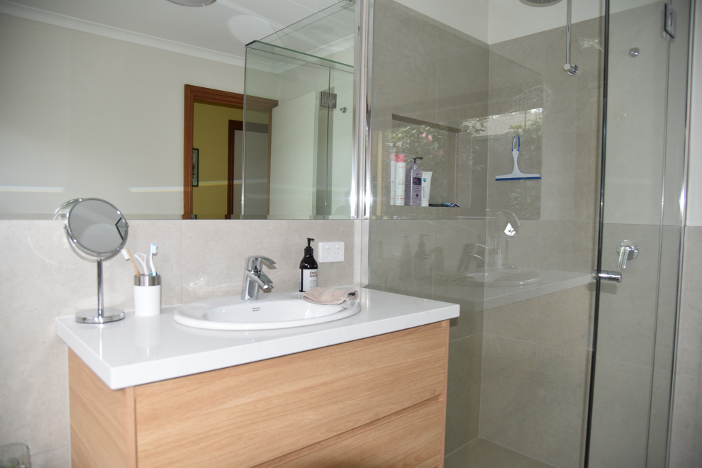 This is an example of a mid-sized contemporary master bathroom in Melbourne with flat-panel cabinets, medium wood cabinets, a drop-in tub, a corner shower, a two-piece toilet, beige tile, ceramic tile, white walls, ceramic floors, a drop-in sink, solid surface benchtops, beige floor, a hinged shower door, white benchtops, a niche, a single vanity and a freestanding vanity.