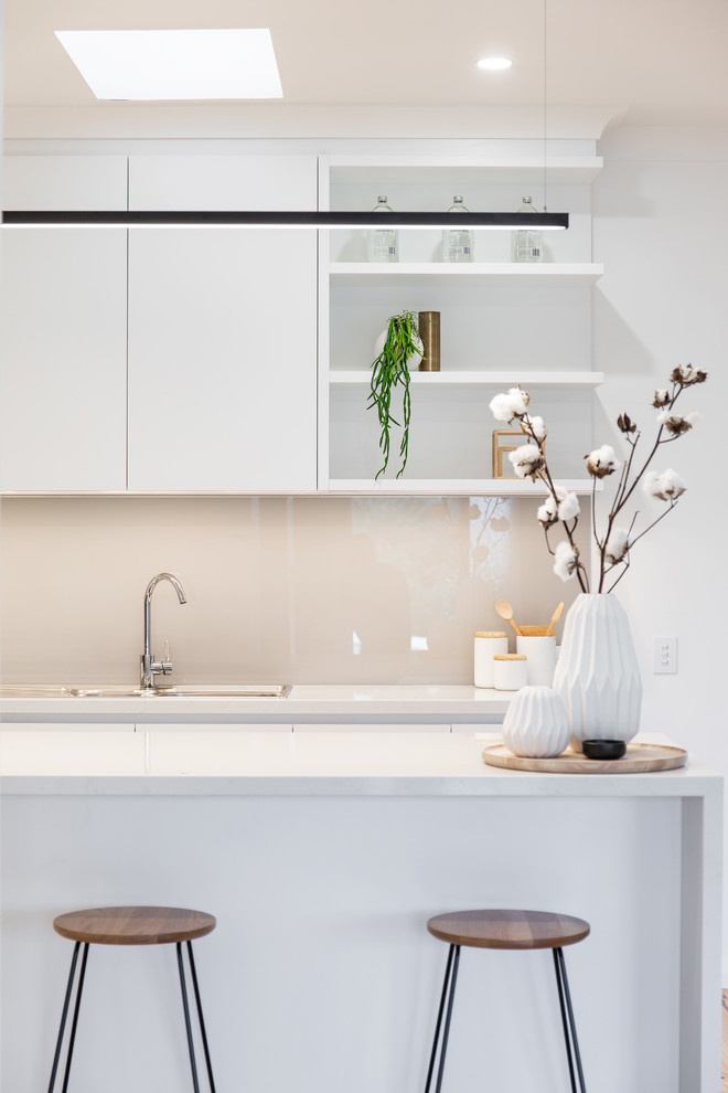 Inspiration for a contemporary l-shaped kitchen pantry in Adelaide with a drop-in sink, flat-panel cabinets, white cabinets, quartz benchtops, grey splashback, glass sheet splashback, stainless steel appliances, light hardwood floors, with island, brown floor and white benchtop.