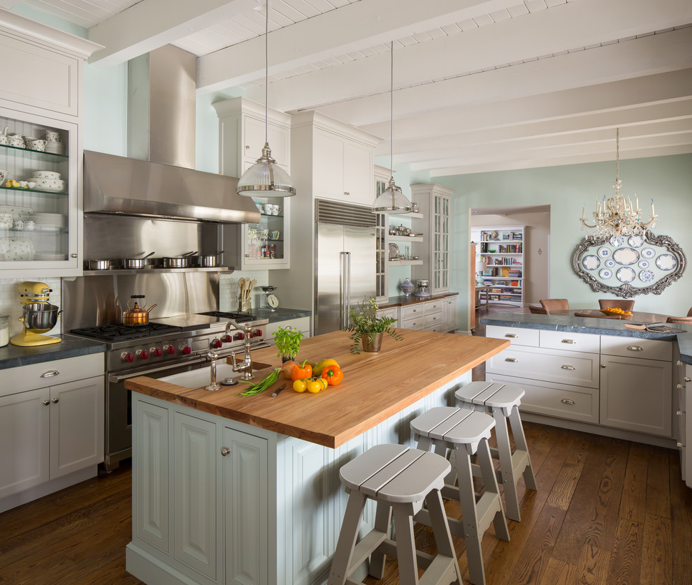 Design ideas for a traditional galley eat-in kitchen in Los Angeles with a farmhouse sink, glass-front cabinets, white cabinets, wood benchtops, metallic splashback, stainless steel appliances, medium hardwood floors and with island.