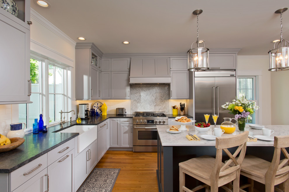 This is an example of a large transitional u-shaped eat-in kitchen in Boston with a farmhouse sink, shaker cabinets, grey cabinets, granite benchtops, white splashback, stainless steel appliances, with island and black benchtop.