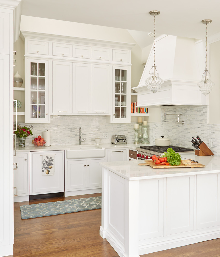 This is an example of a transitional u-shaped kitchen in Boston with a farmhouse sink, beaded inset cabinets, white cabinets, stainless steel appliances, medium hardwood floors, a peninsula, brown floor and white benchtop.