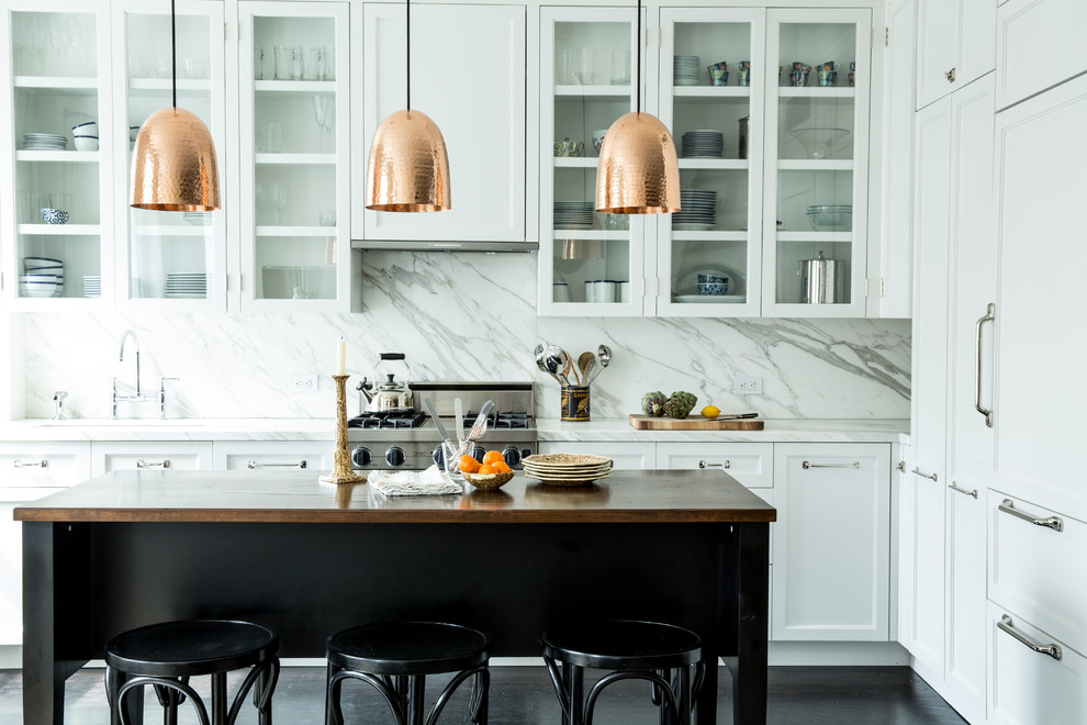 This is an example of a transitional l-shaped kitchen in New York with glass-front cabinets, white cabinets, white splashback, panelled appliances, dark hardwood floors, with island and marble splashback.