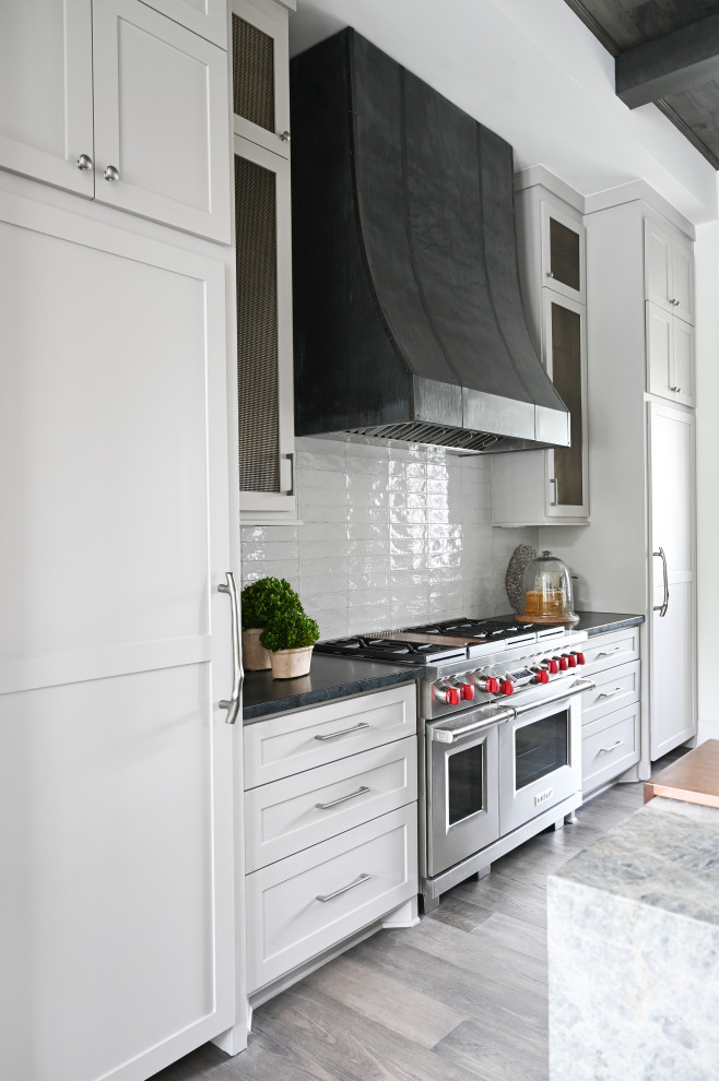 Idéer för mellanstora industriella linjära grått kök med öppen planlösning, med en rustik diskho, luckor med infälld panel, vita skåp, bänkskiva i kvartsit, grått stänkskydd, stänkskydd i keramik, rostfria vitvaror, mörkt trägolv, en köksö och brunt golv