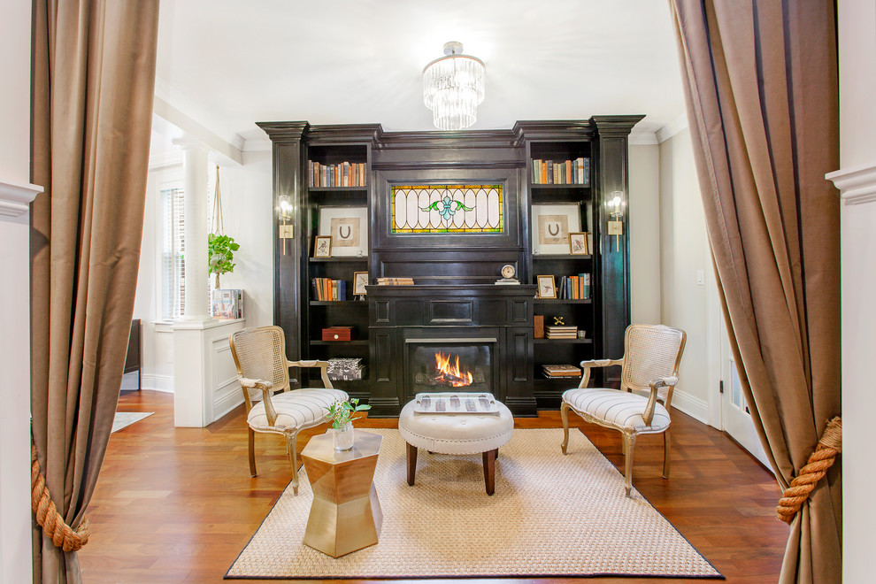 Photo of a mid-sized traditional enclosed living room in New York with a library, white walls, medium hardwood floors, a standard fireplace, a wood fireplace surround, no tv and black floor.