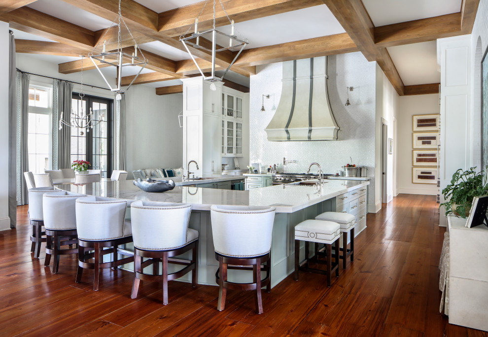 Inspiration for an expansive transitional u-shaped open plan kitchen in New Orleans with an undermount sink, white cabinets, white splashback, stainless steel appliances, medium hardwood floors, with island, brown floor, white benchtop, exposed beam and beaded inset cabinets.