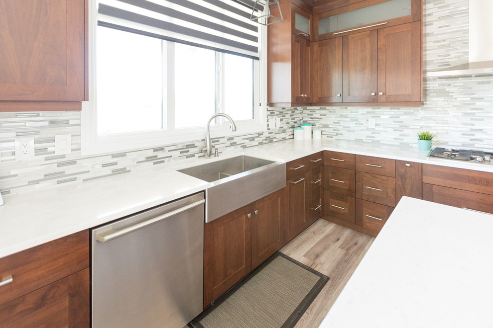 Transitional l-shaped beige floor open concept kitchen photo with a farmhouse sink, recessed-panel cabinets, medium tone wood cabinets, gray backsplash, mosaic tile backsplash, stainless steel appliances and an island
