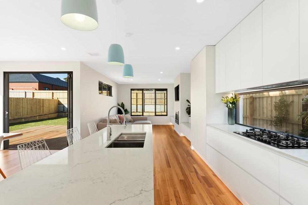 Inspiration for a large contemporary eat-in kitchen in Geelong with an integrated sink, white splashback, glass sheet splashback, stainless steel appliances, medium hardwood floors, with island, brown floor and white benchtop.