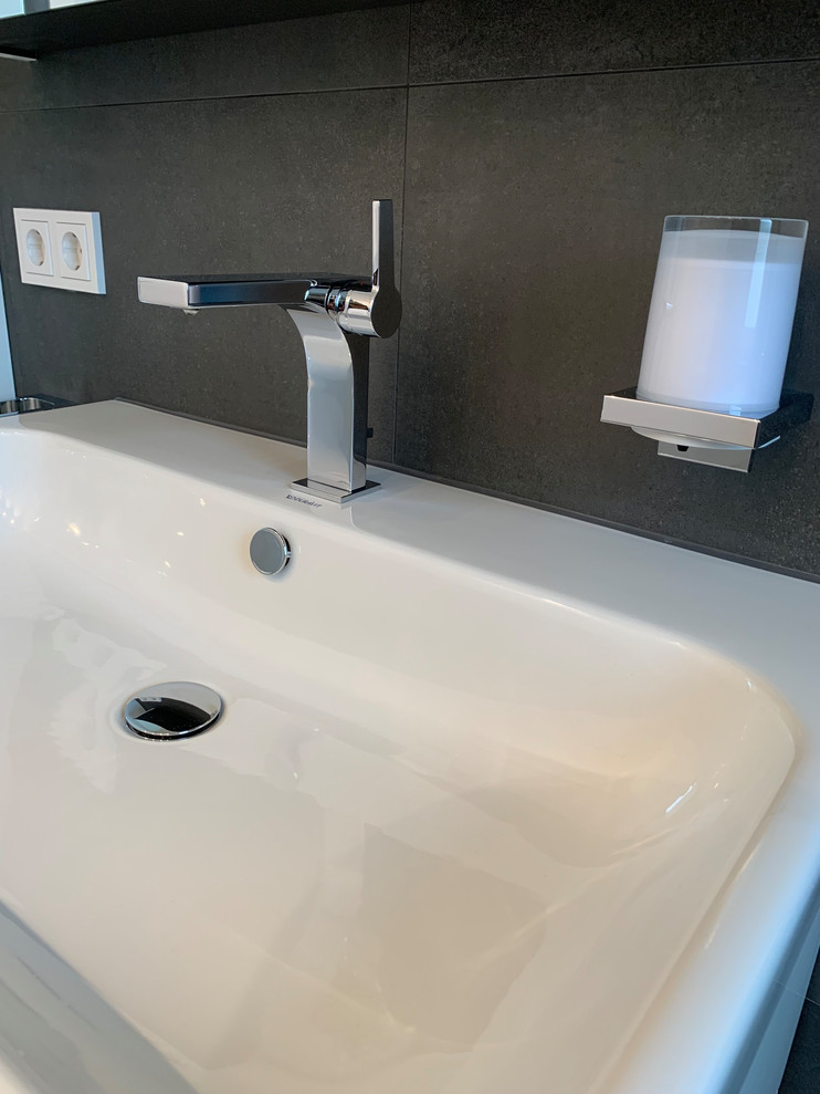 Duschbad With flächenbündigen Schrankfronten, weißen Schränken, Duschnische, Wandtoilette, schwarzen Fliesen, weißer Wandfarbe, Wandwaschbecken, schwarzem Boden and offener Dusche in Munich