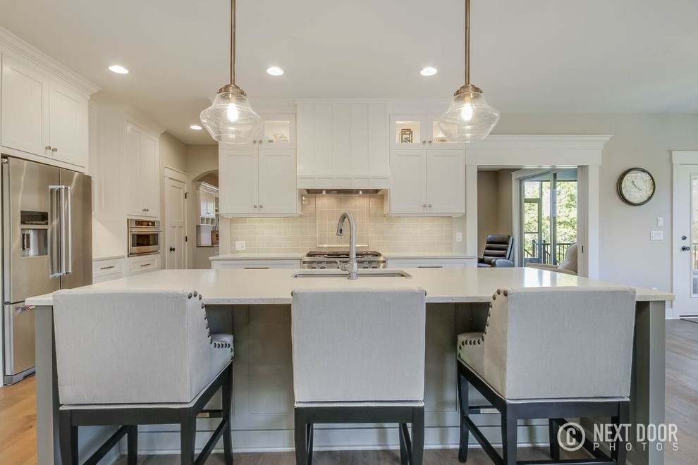 Open concept kitchen - mid-sized transitional u-shaped open concept kitchen idea in Grand Rapids with an undermount sink, shaker cabinets, white cabinets, solid surface countertops, beige backsplash, ceramic backsplash and an island