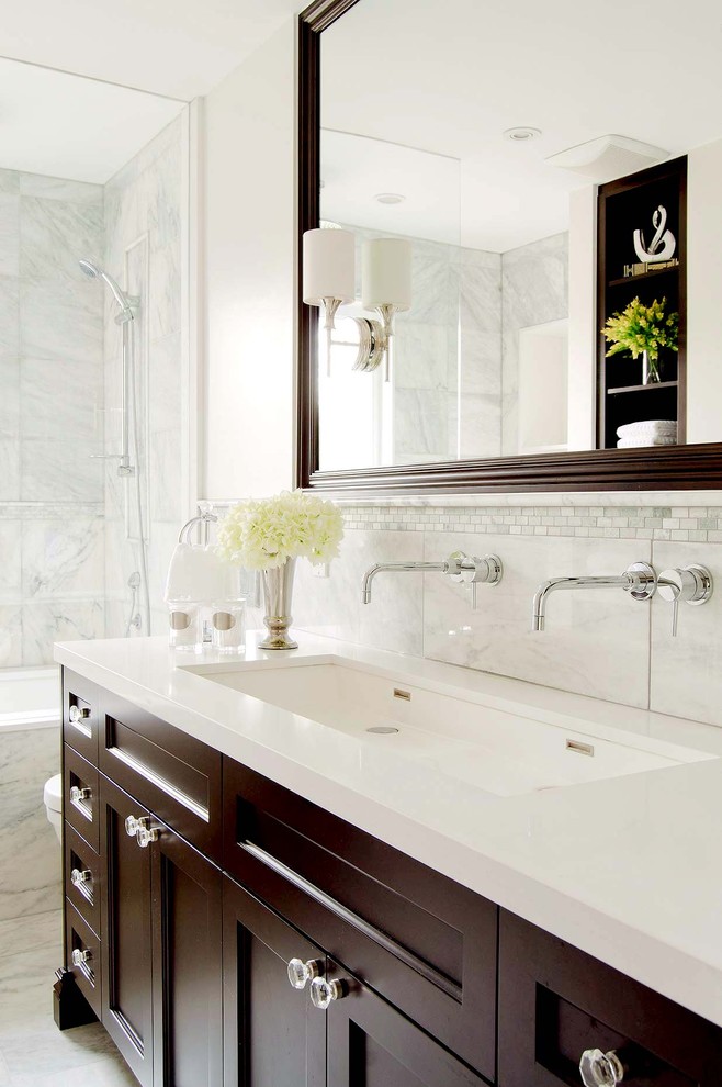 This is an example of a traditional bathroom in Toronto with recessed-panel cabinets, dark wood cabinets, an alcove tub, a shower/bathtub combo, white tile, a trough sink and white benchtops.