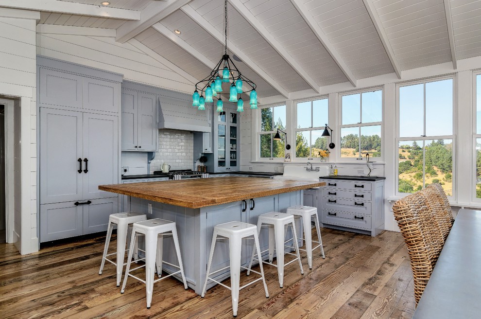 Beach style l-shaped eat-in kitchen in San Francisco with a farmhouse sink, shaker cabinets, white splashback, subway tile splashback, panelled appliances, medium hardwood floors, with island and grey cabinets.