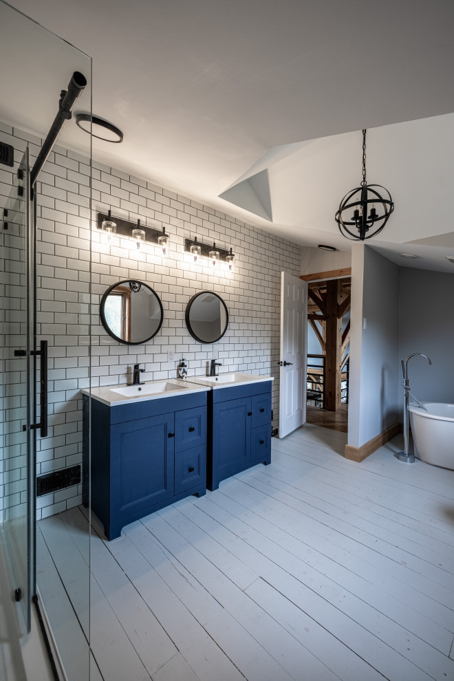 Пример оригинального дизайна: большая главная ванная комната в стиле кантри с фасадами в стиле шейкер, синими фасадами, отдельно стоящей ванной, угловым душем, раздельным унитазом, белой плиткой, плиткой кабанчик, серыми стенами, деревянным полом, монолитной раковиной, столешницей из искусственного камня, серым полом, душем с раздвижными дверями, белой столешницей, тумбой под одну раковину, напольной тумбой и сводчатым потолком