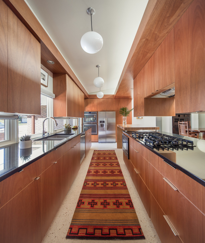 Photo of a small midcentury galley separate kitchen in Denver with flat-panel cabinets, medium wood cabinets, granite benchtops, terrazzo floors, a peninsula, black benchtop, a double-bowl sink, window splashback, stainless steel appliances and white floor.