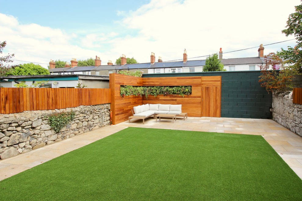 This is an example of a mid-sized contemporary backyard full sun formal garden for summer in Dublin with a vertical garden, natural stone pavers and a stone fence.