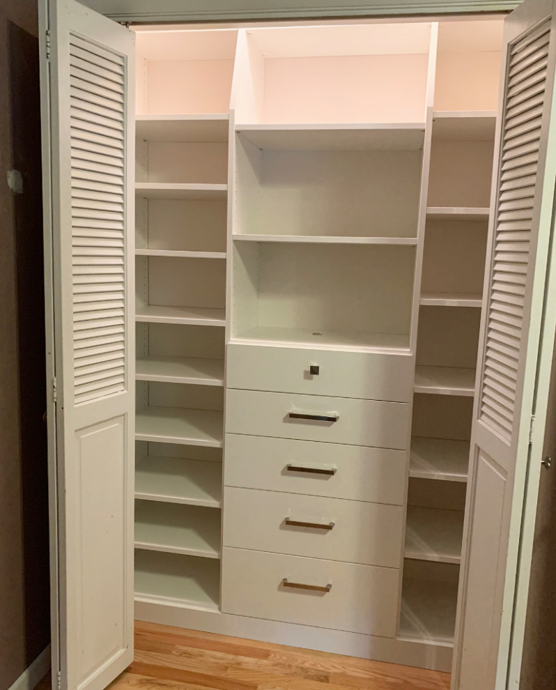 Inspiration for a small traditional gender-neutral built-in wardrobe in Other with flat-panel cabinets, white cabinets, light hardwood floors and yellow floor.