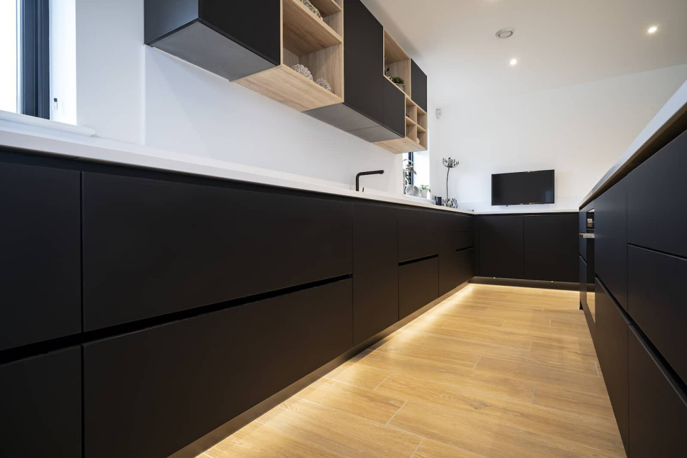 Inspiration for a large scandinavian l-shaped open plan kitchen in Oxfordshire with flat-panel cabinets, black cabinets, quartzite benchtops, white splashback, black appliances, light hardwood floors, with island, brown floor and yellow benchtop.