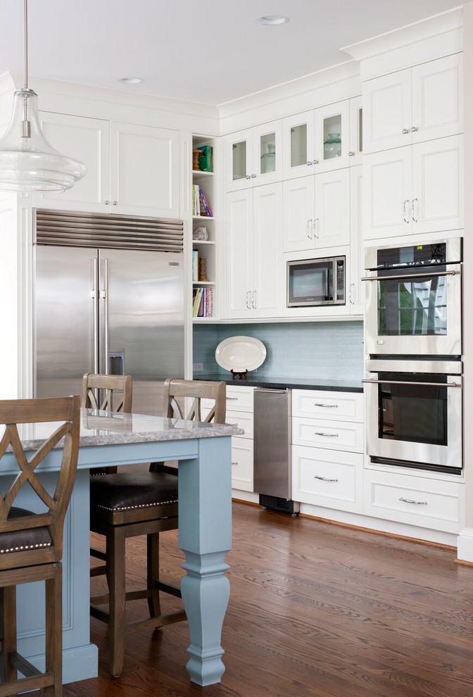 Mid-sized transitional l-shaped medium tone wood floor open concept kitchen photo in DC Metro with a farmhouse sink, beaded inset cabinets, white cabinets, limestone countertops, blue backsplash, matchstick tile backsplash, stainless steel appliances and an island