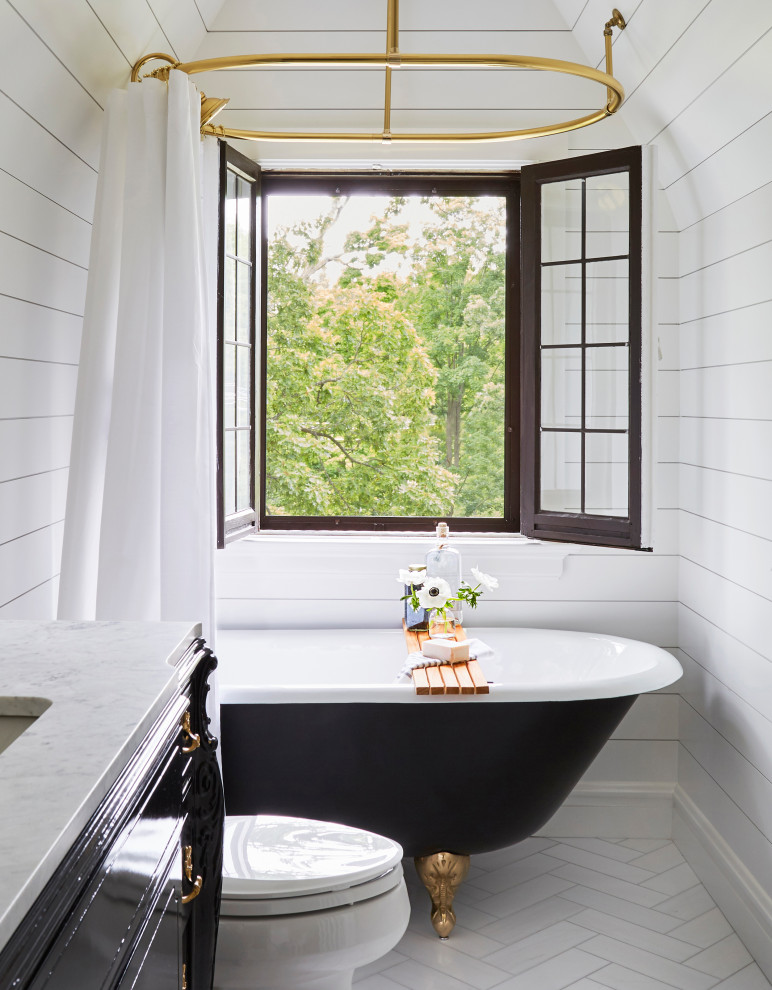 This is an example of a small traditional bathroom in Chicago with black cabinets, a claw-foot tub, a shower/bathtub combo, a one-piece toilet, white walls, marble floors, an undermount sink, marble benchtops, white floor, a shower curtain, white benchtops, a single vanity, a freestanding vanity, vaulted, planked wall panelling and recessed-panel cabinets.