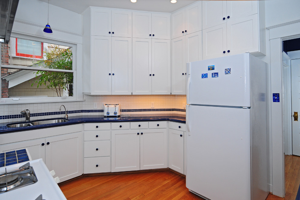 Mid-sized transitional u-shaped medium tone wood floor kitchen pantry photo in Seattle with a double-bowl sink, shaker cabinets, white cabinets, solid surface countertops, blue backsplash, ceramic backsplash, white appliances, white walls and no island