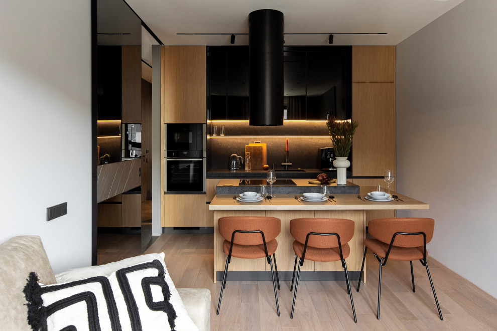 Mid-sized contemporary single-wall eat-in kitchen in Moscow with a single-bowl sink, glass-front cabinets, medium wood cabinets, black splashback, engineered quartz splashback, black appliances, medium hardwood floors, with island and beige floor.