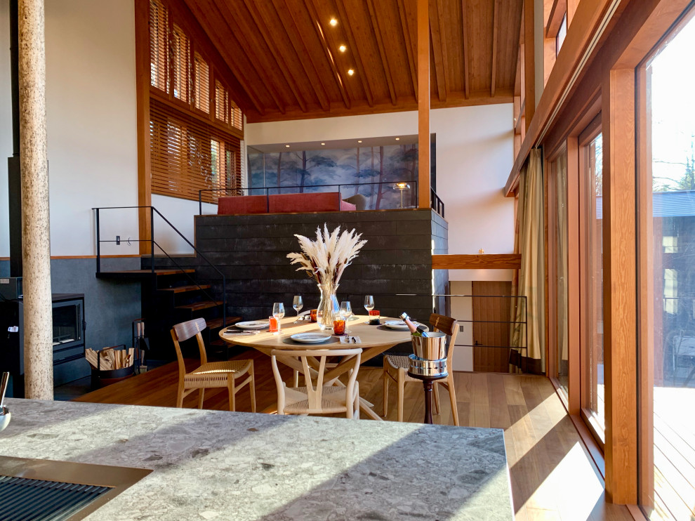 Foto di una grande sala da pranzo aperta verso la cucina con pareti bianche, pavimento in legno massello medio, stufa a legna, cornice del camino piastrellata e pavimento marrone