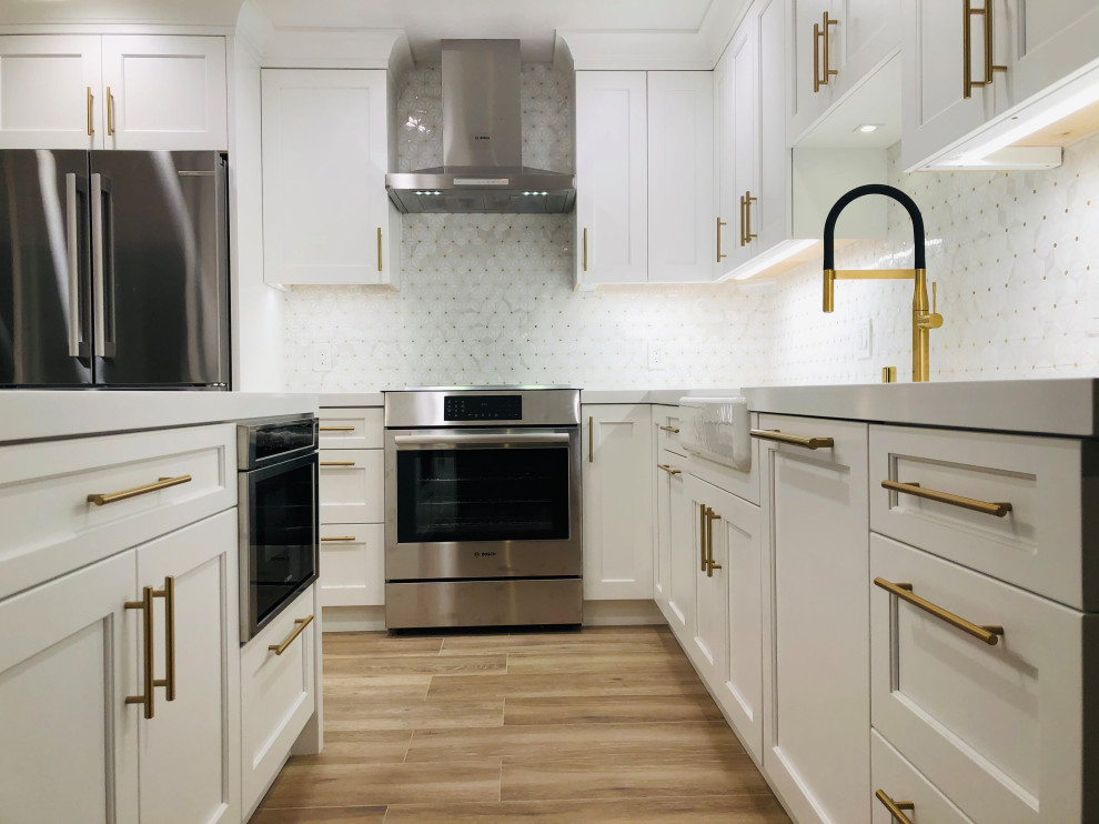 Example of a mid-sized transitional l-shaped medium tone wood floor and brown floor eat-in kitchen design in San Francisco with a farmhouse sink, recessed-panel cabinets, white cabinets, quartz countertops, white backsplash, mosaic tile backsplash, stainless steel appliances, a peninsula and white countertops