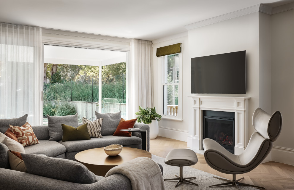 Идея дизайна: большая открытая гостиная комната в стиле неоклассика (современная классика) с белыми стенами, светлым паркетным полом, двусторонним камином, фасадом камина из дерева, коричневым полом и тюлем на окнах