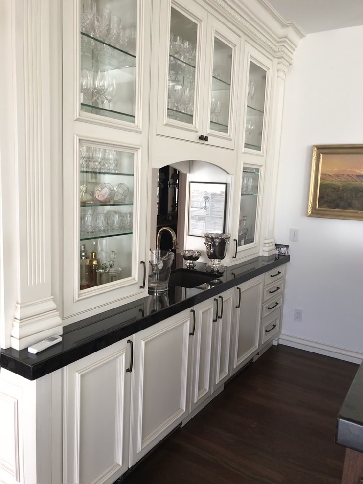 Design ideas for a large transitional galley seated home bar in Denver with an undermount sink, glass-front cabinets, white cabinets, solid surface benchtops, dark hardwood floors and brown floor.