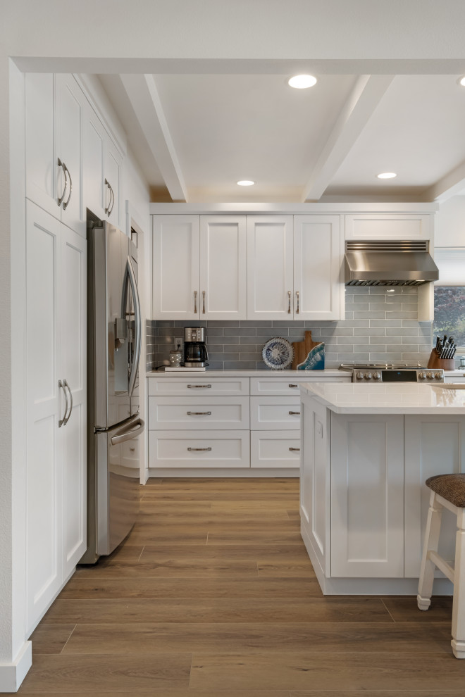 Design ideas for a mid-sized beach style galley eat-in kitchen in Seattle with a drop-in sink, beaded inset cabinets, white cabinets, marble benchtops, grey splashback, ceramic splashback, stainless steel appliances, vinyl floors, multiple islands, brown floor, white benchtop and coffered.