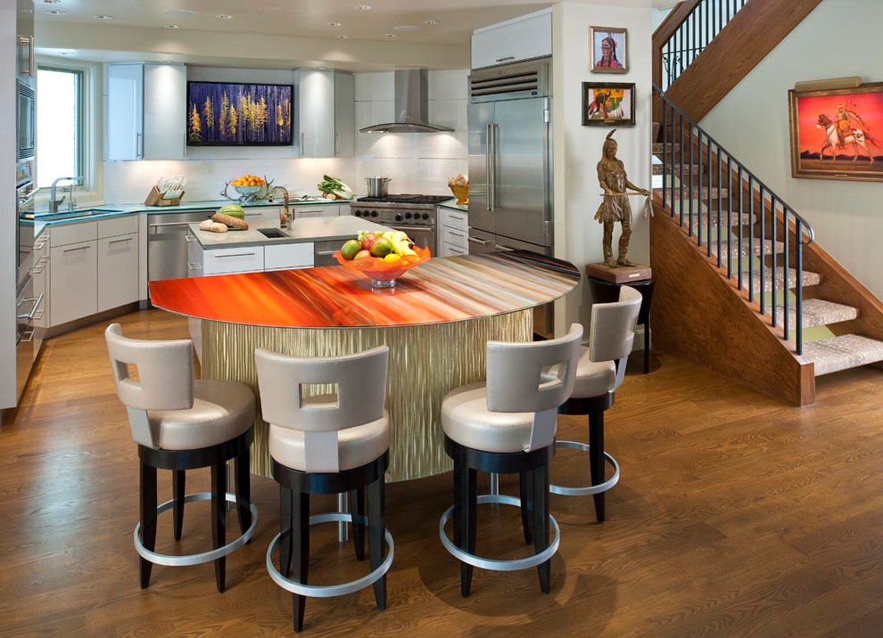 Inspiration for a large country single-wall eat-in kitchen in Denver with an undermount sink, flat-panel cabinets, white cabinets, glass benchtops, white splashback, glass tile splashback, stainless steel appliances, medium hardwood floors and multiple islands.