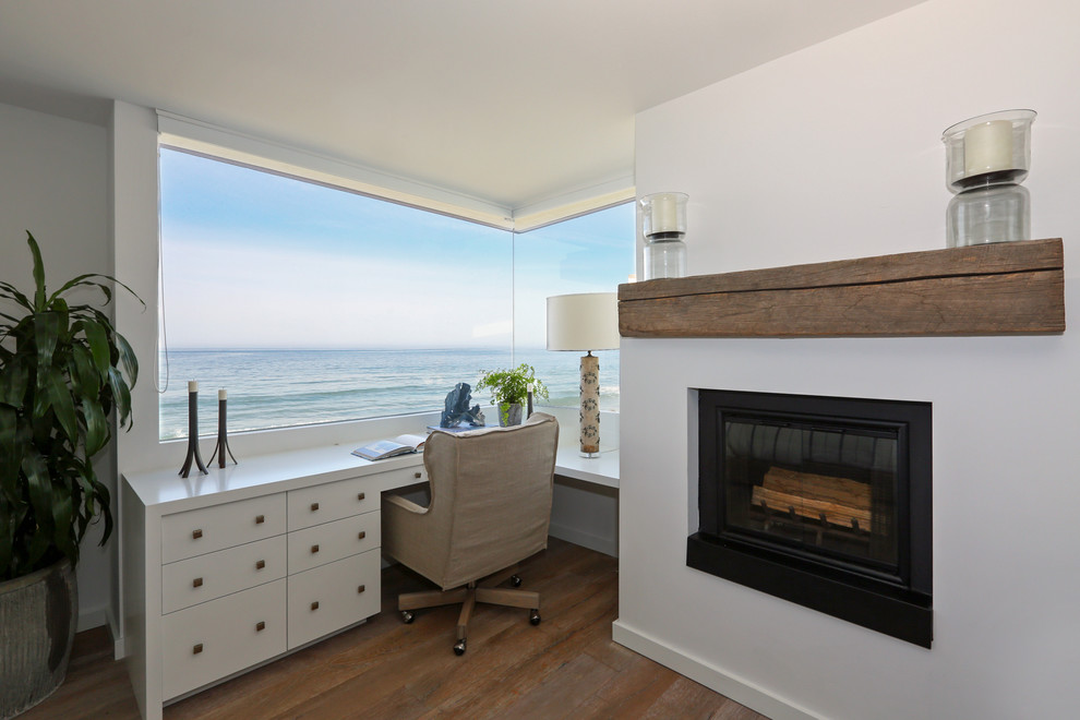 Design ideas for a beach style home office in Santa Barbara with white walls, dark hardwood floors, a standard fireplace and a built-in desk.