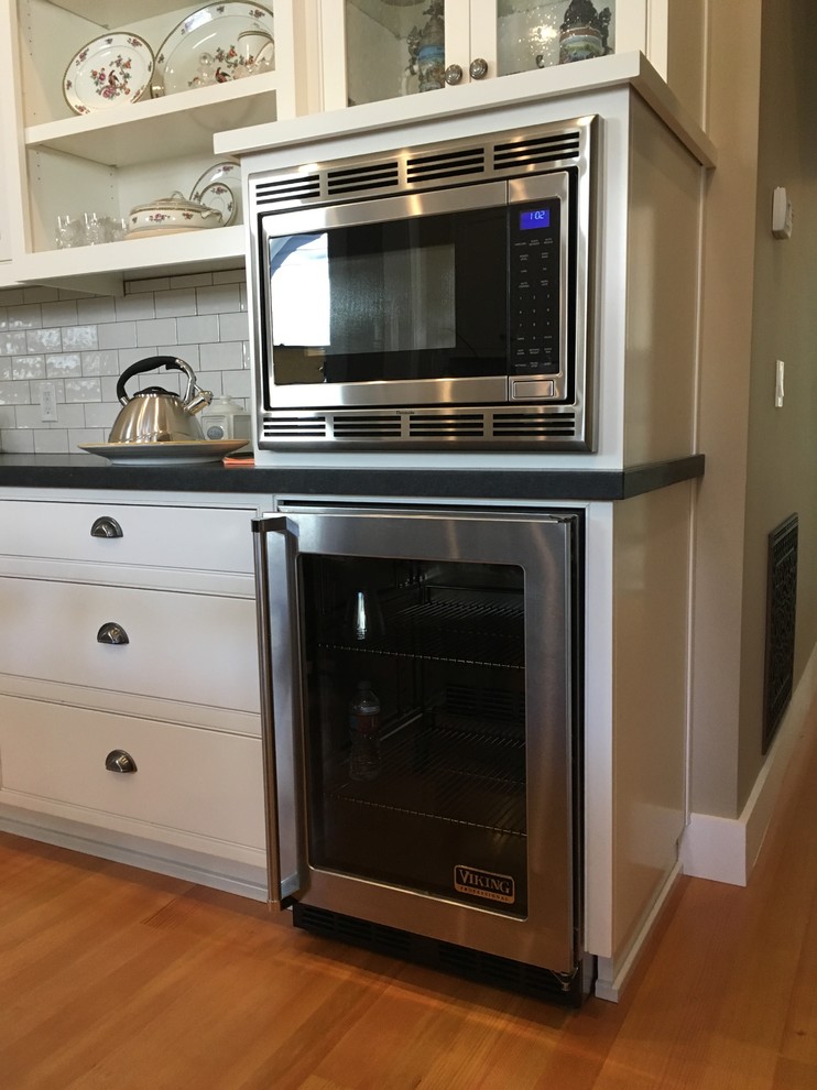 Example of a mid-sized transitional l-shaped medium tone wood floor and brown floor enclosed kitchen design in Phoenix with stainless steel appliances, glass-front cabinets, white cabinets, solid surface countertops, gray backsplash and subway tile backsplash