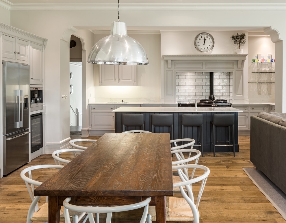 Inspiration for a mid-sized transitional kitchen in Manchester with raised-panel cabinets, grey cabinets, white splashback, stainless steel appliances, with island, white benchtop, subway tile splashback, medium hardwood floors and brown floor.