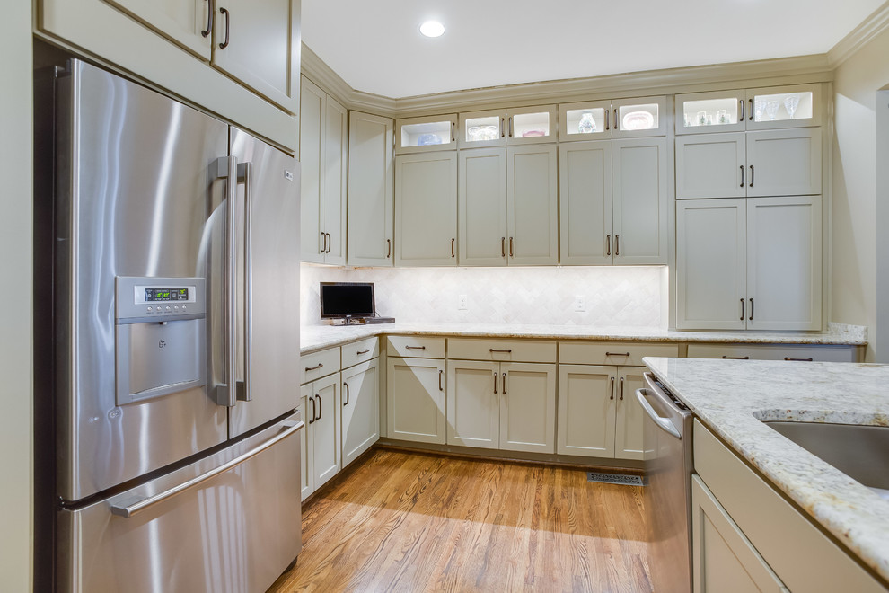 Inspiration for a transitional u-shaped medium tone wood floor and brown floor enclosed kitchen remodel in Birmingham with a double-bowl sink, shaker cabinets, beige cabinets, granite countertops, beige backsplash, travertine backsplash, stainless steel appliances and an island