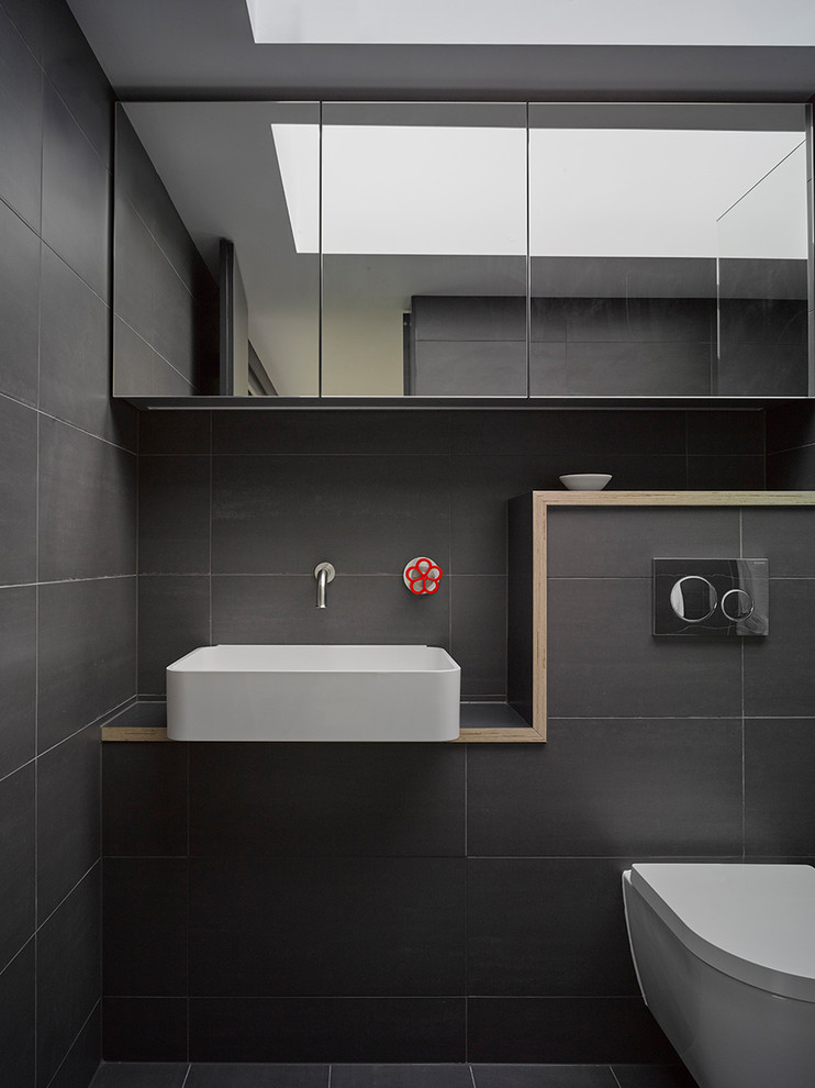 Industrial bathroom in London with a wall-mount toilet, gray tile and a vessel sink.