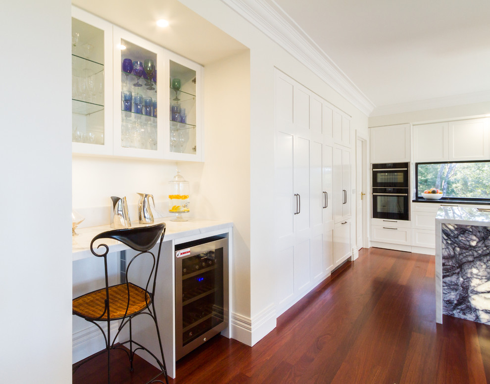 Photo of a large contemporary u-shaped eat-in kitchen in Melbourne with an undermount sink, shaker cabinets, white cabinets, marble benchtops, white splashback, window splashback, black appliances, dark hardwood floors, with island, brown floor and white benchtop.