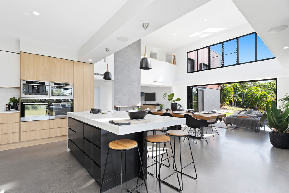 Design ideas for a large contemporary open plan kitchen in Sunshine Coast with light wood cabinets, stainless steel appliances, concrete floors, with island, grey floor, a drop-in sink, quartz benchtops, white splashback and flat-panel cabinets.