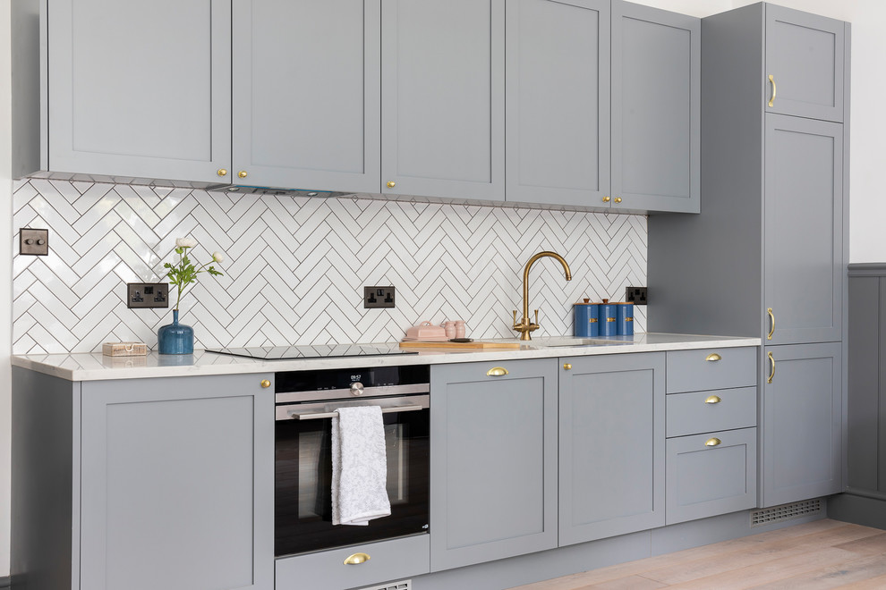 Design ideas for a small transitional single-wall eat-in kitchen in Hertfordshire with an undermount sink, shaker cabinets, grey cabinets, quartzite benchtops, white splashback, mosaic tile splashback, black appliances, porcelain floors, no island, grey floor and white benchtop.