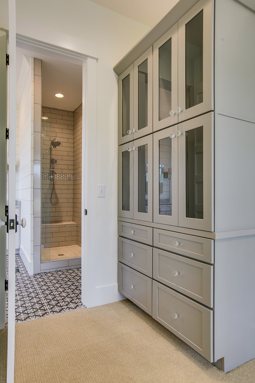 Mid-sized country gender-neutral walk-in wardrobe in Nashville with glass-front cabinets, grey cabinets and carpet.