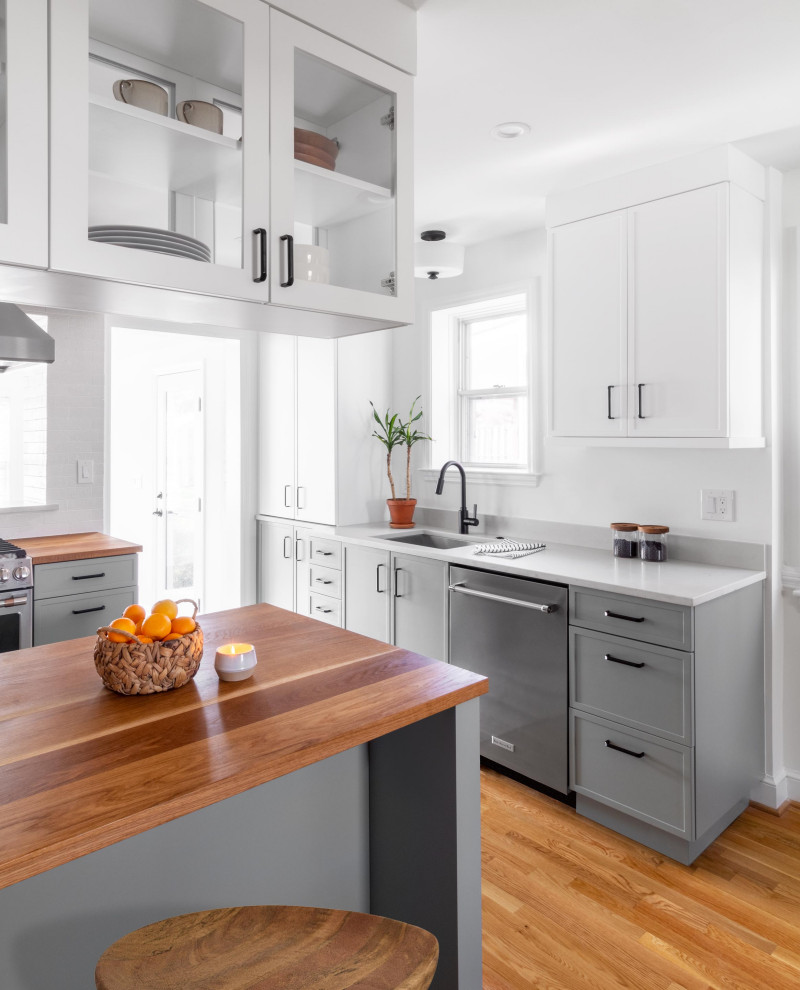 Inspiration for a mid-sized transitional l-shaped eat-in kitchen in DC Metro with an undermount sink, shaker cabinets, green cabinets, wood benchtops, white splashback, subway tile splashback, stainless steel appliances, light hardwood floors, a peninsula, brown floor and brown benchtop.