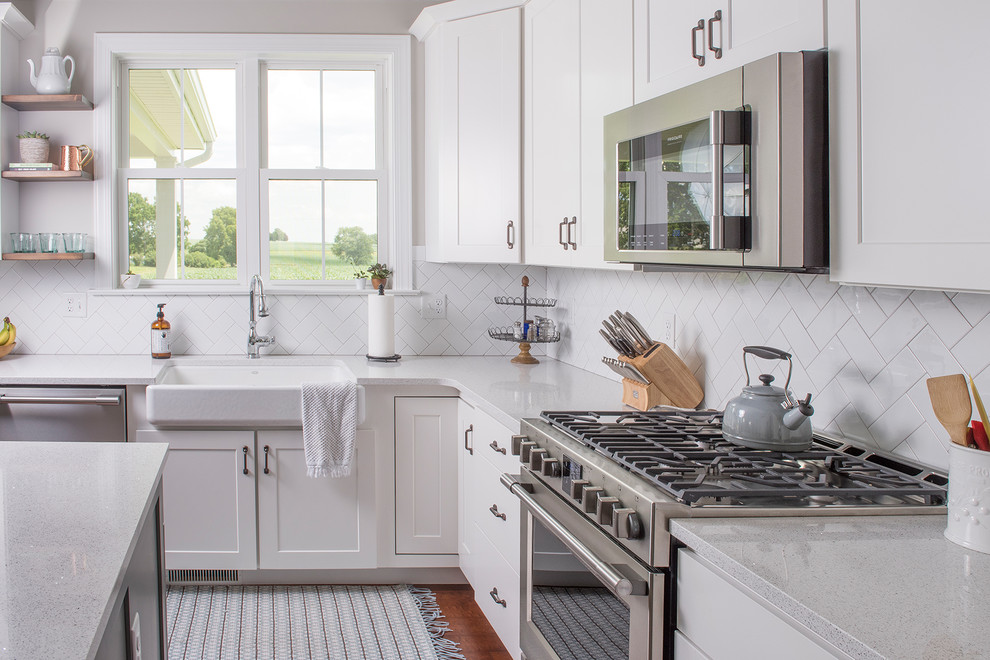 Mid-sized transitional l-shaped medium tone wood floor and brown floor open concept kitchen photo with a farmhouse sink, shaker cabinets, white cabinets, quartzite countertops, white backsplash, subway tile backsplash, paneled appliances and an island
