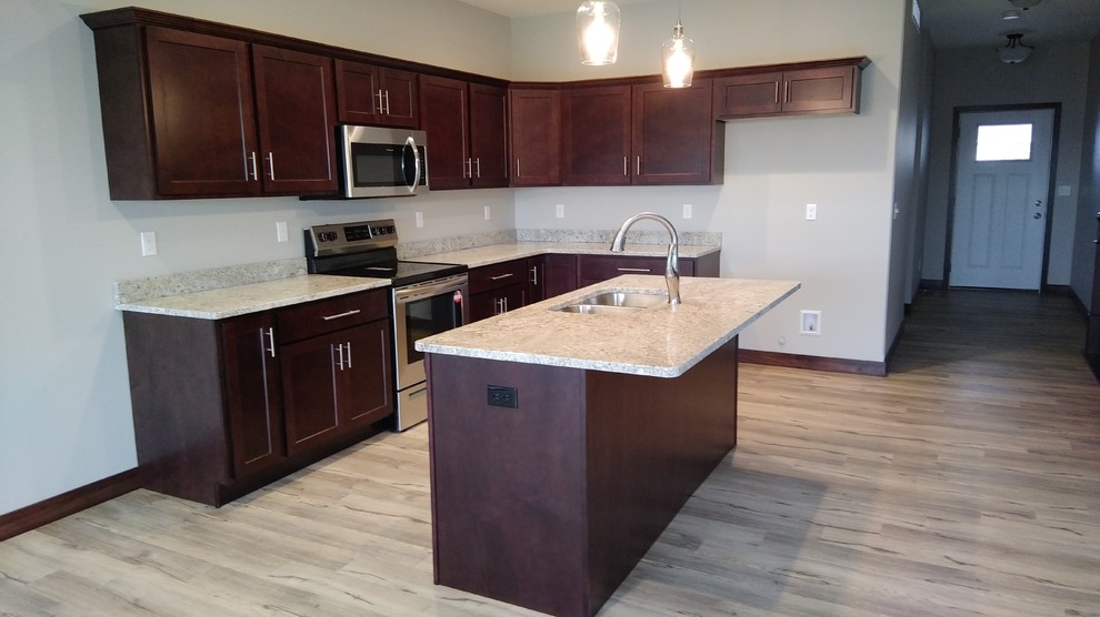 This is an example of a mid-sized transitional l-shaped eat-in kitchen in Cedar Rapids with a double-bowl sink, shaker cabinets, brown cabinets, granite benchtops, stainless steel appliances, vinyl floors, with island and grey floor.