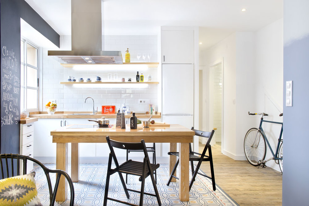 Small transitional l-shaped open plan kitchen in Madrid with a drop-in sink, flat-panel cabinets, white splashback, subway tile splashback, white appliances, medium hardwood floors, no island, white cabinets and wood benchtops.