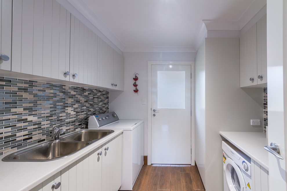 Photo of a small contemporary galley dedicated laundry room in Sydney with a double-bowl sink, recessed-panel cabinets, white cabinets, laminate benchtops, medium hardwood floors and grey walls.