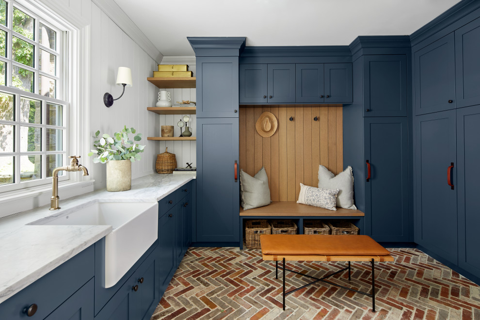 This is an example of a transitional u-shaped utility room in New York with a farmhouse sink, shaker cabinets, blue cabinets, marble benchtops, white splashback, white walls, brick floors, multi-coloured floor, multi-coloured benchtop and panelled walls.