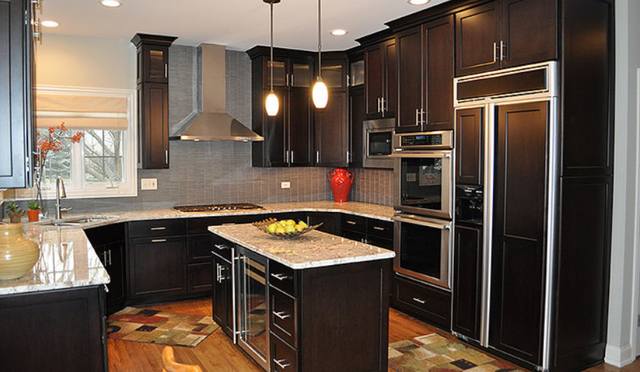 Kitchen - mid-sized transitional u-shaped medium tone wood floor and brown floor kitchen idea in Chicago with an undermount sink, recessed-panel cabinets, dark wood cabinets, granite countertops, gray backsplash, paneled appliances, an island and multicolored countertops