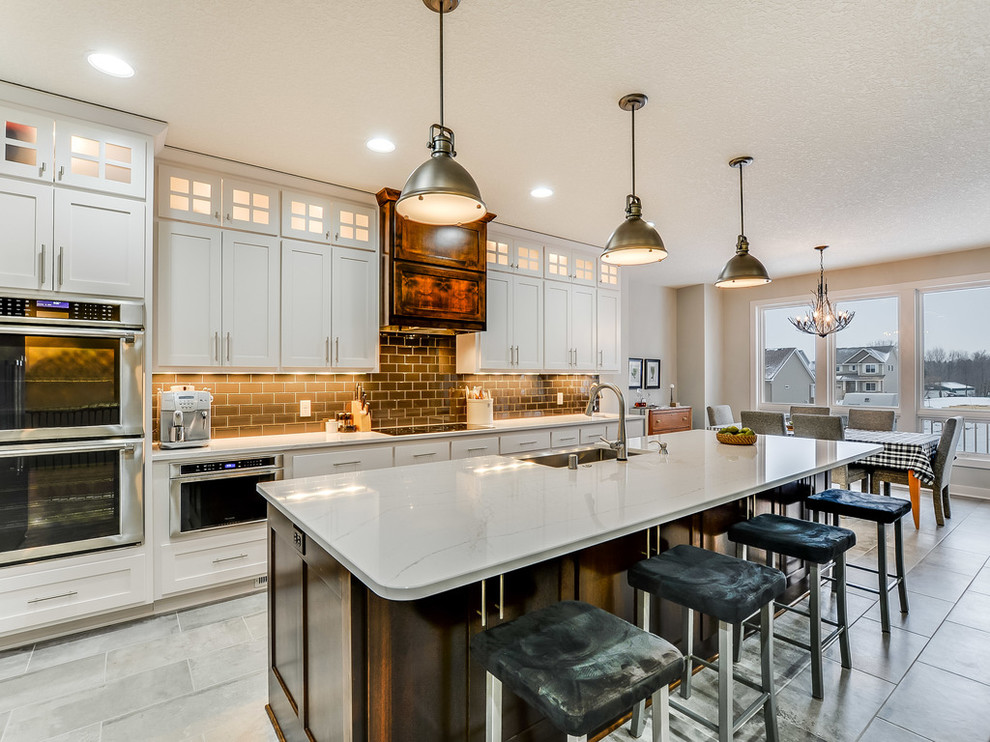 This is an example of an eclectic galley open plan kitchen in Minneapolis with a farmhouse sink, shaker cabinets, solid surface benchtops, grey splashback, subway tile splashback, stainless steel appliances, porcelain floors and with island.